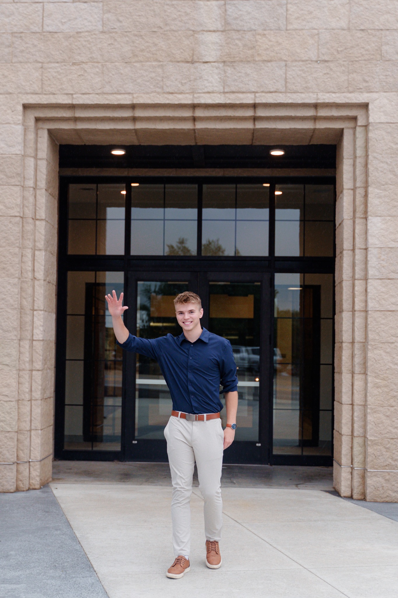 Logan smiling and waving hello outside a building